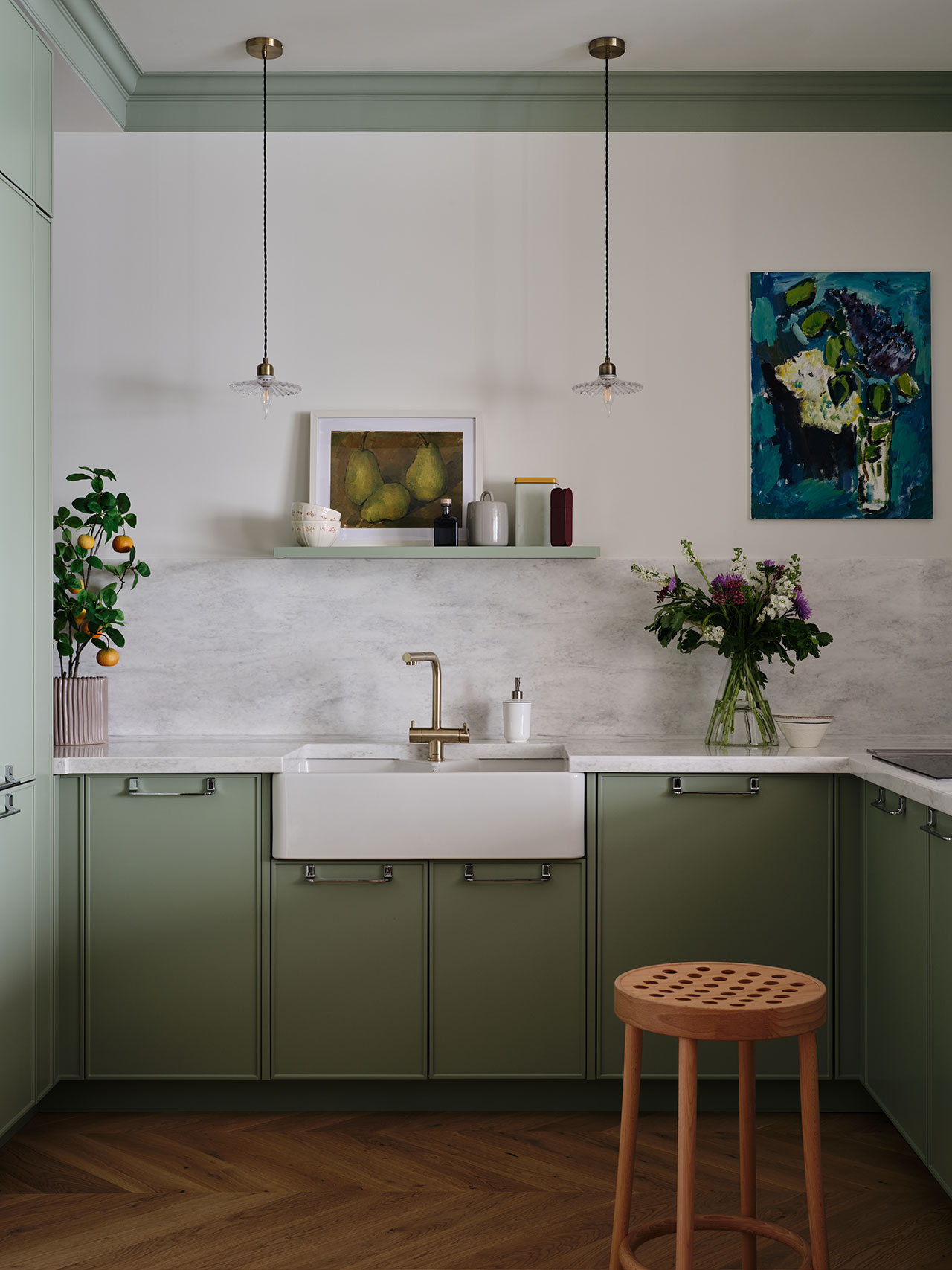 Close-up of sage green kitchen cabinets with a marble backsplash and a white farmhouse sink.