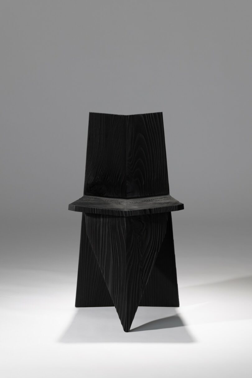 A black angular wooden chair centered against a neutral gray background.