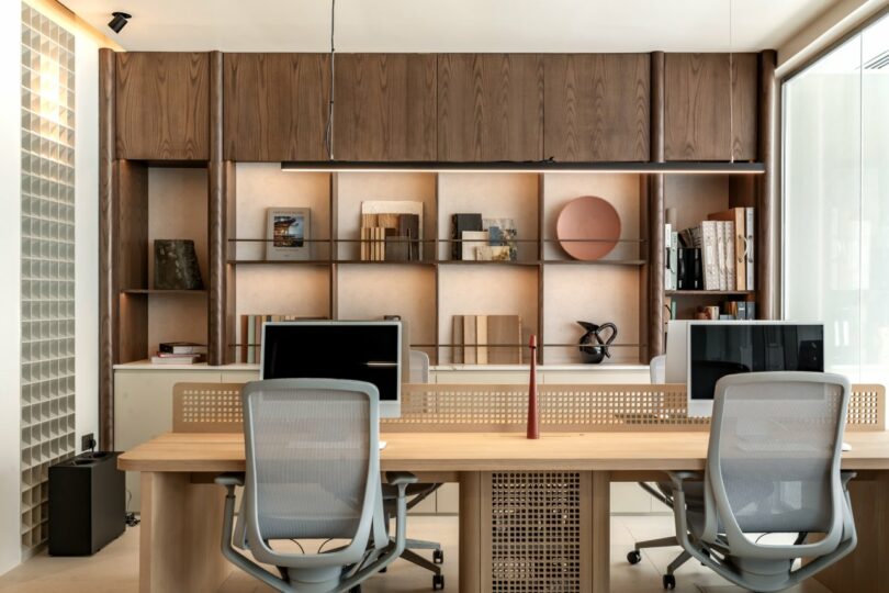 Bright office workstations with wooden desks, ergonomic chairs, and large windows.