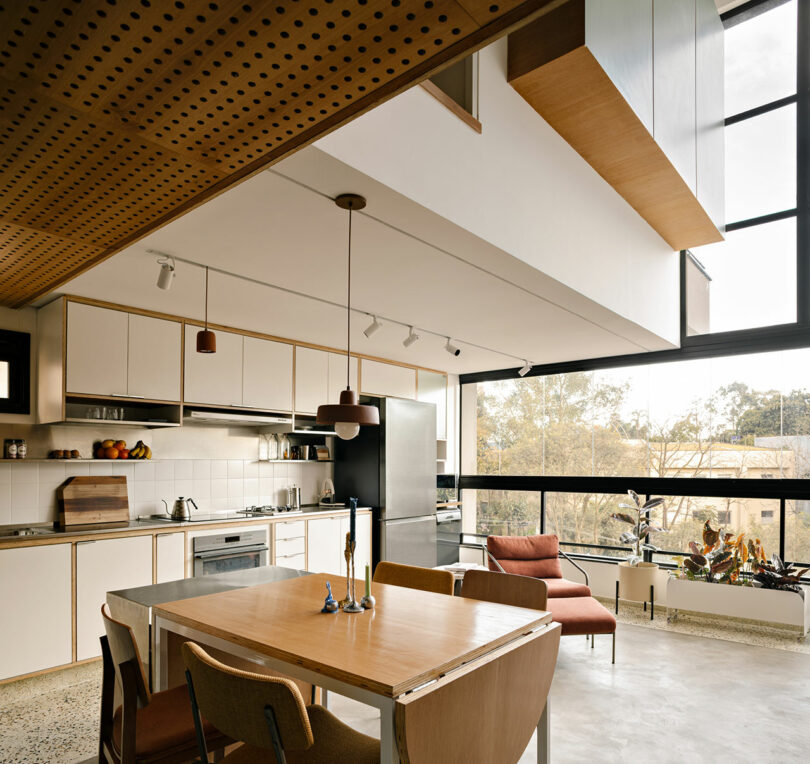 Modern kitchen with wooden cabinets and a large window overlooking trees.