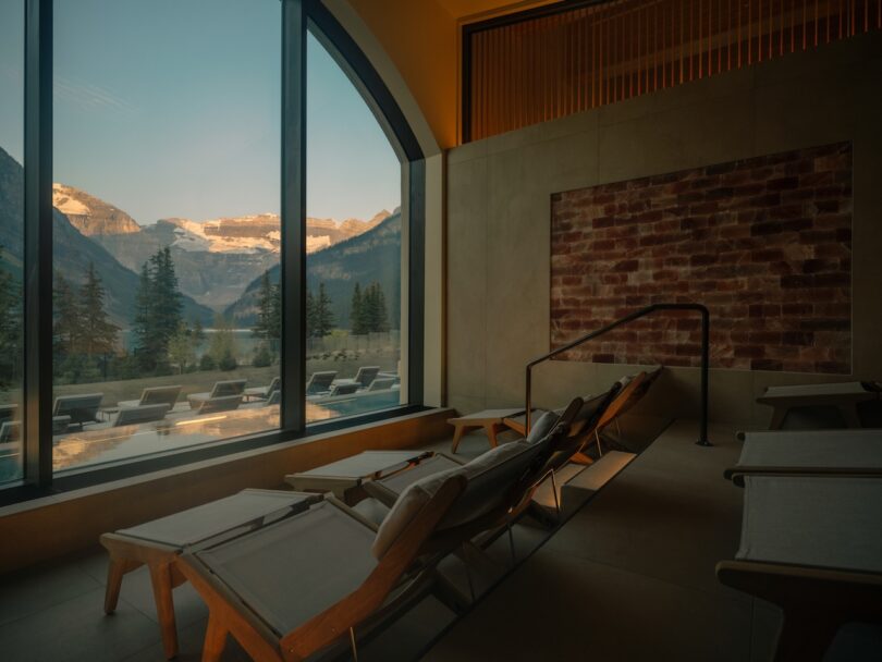 A mountain view at sunset seen through a large window of a modern lounge with brick walls.