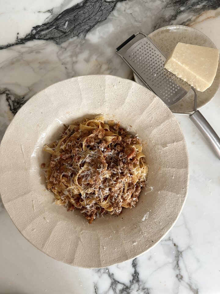 A bowl of wide tagliatelle noodles topped with a rich, slow-simmered meat bolognese sauce.