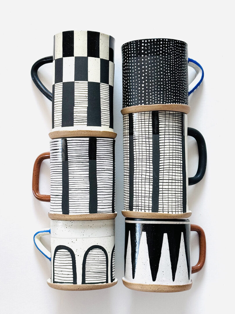Collection of handmade clay mugs with diverse black and white hand-drawn patterns.
