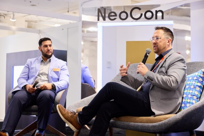 Two speakers on a stage at NeoCon engaged in a professional discussion during a seminar.