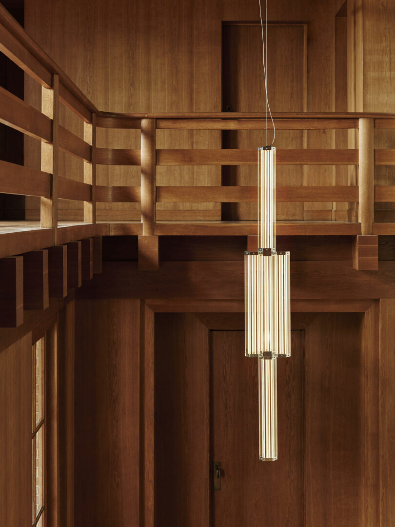 A modern vertical pendant light with cylindrical bulbs hanging in a two-story interior.