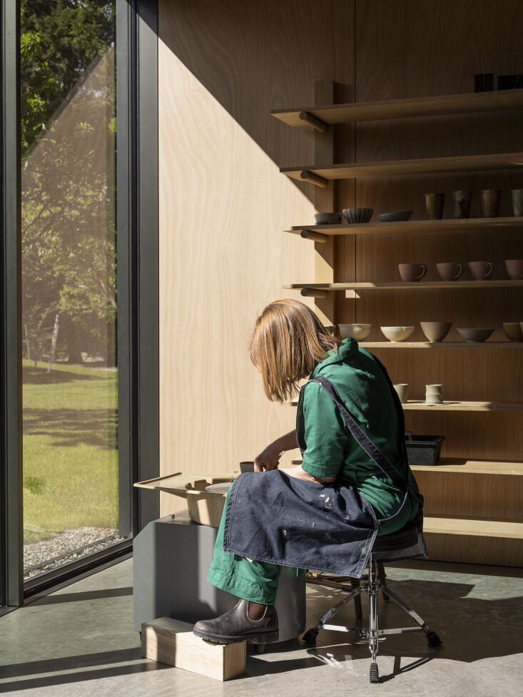 The owner working in a well-lit pottery studio with large windows looking out to the landscape.