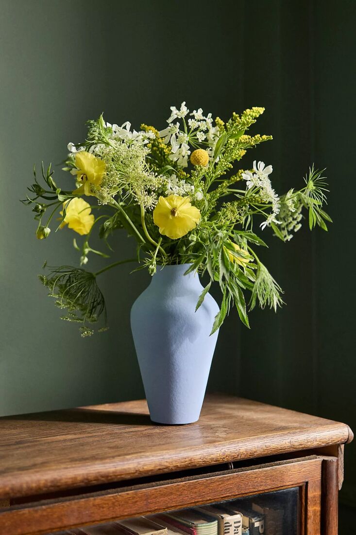 A blue organic ceramic vase sitting on a white workspace shelf.