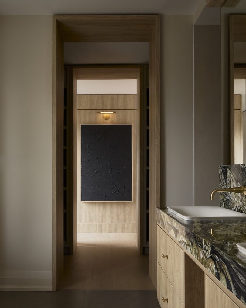 Hallway with wood paneling and black textured artwork leading to a marble bathroom.
