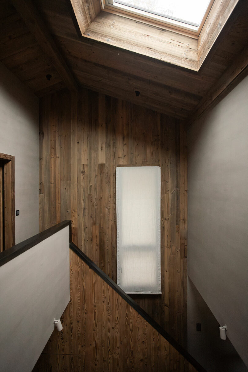 A minimalist wooden staircase landing illuminated by a large overhead skylight.