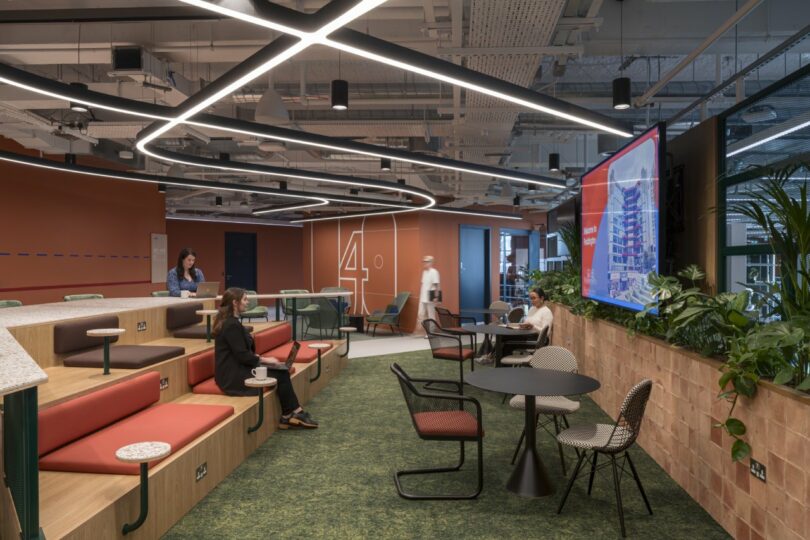 Tiered bleacher-style seating in an office common area with a large screen and indoor plants.