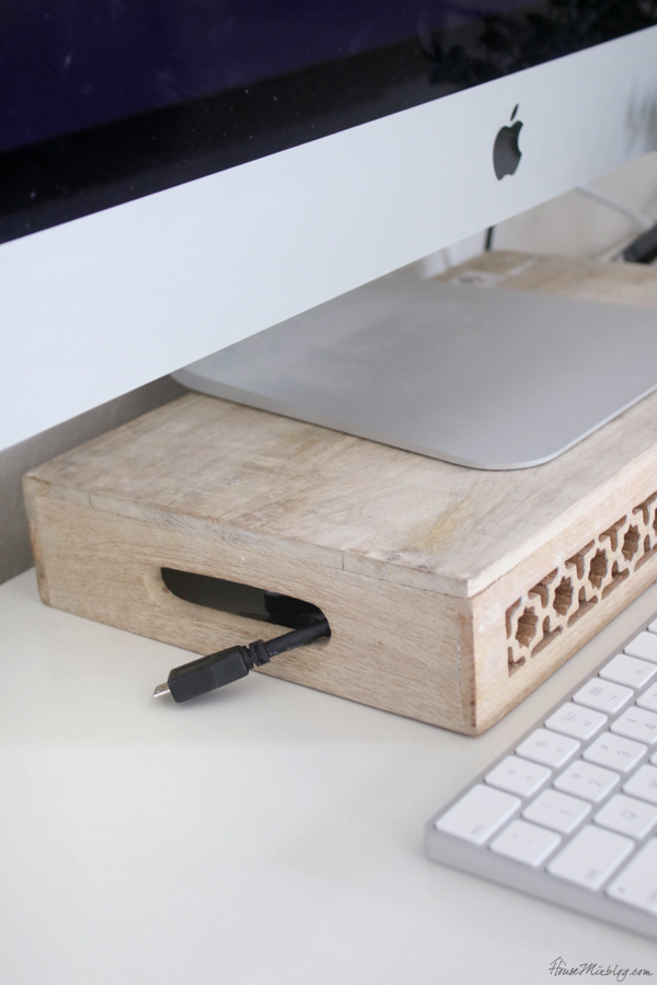 An upside-down wooden crate used as a monitor stand on a white desk, with cords tucked underneath.