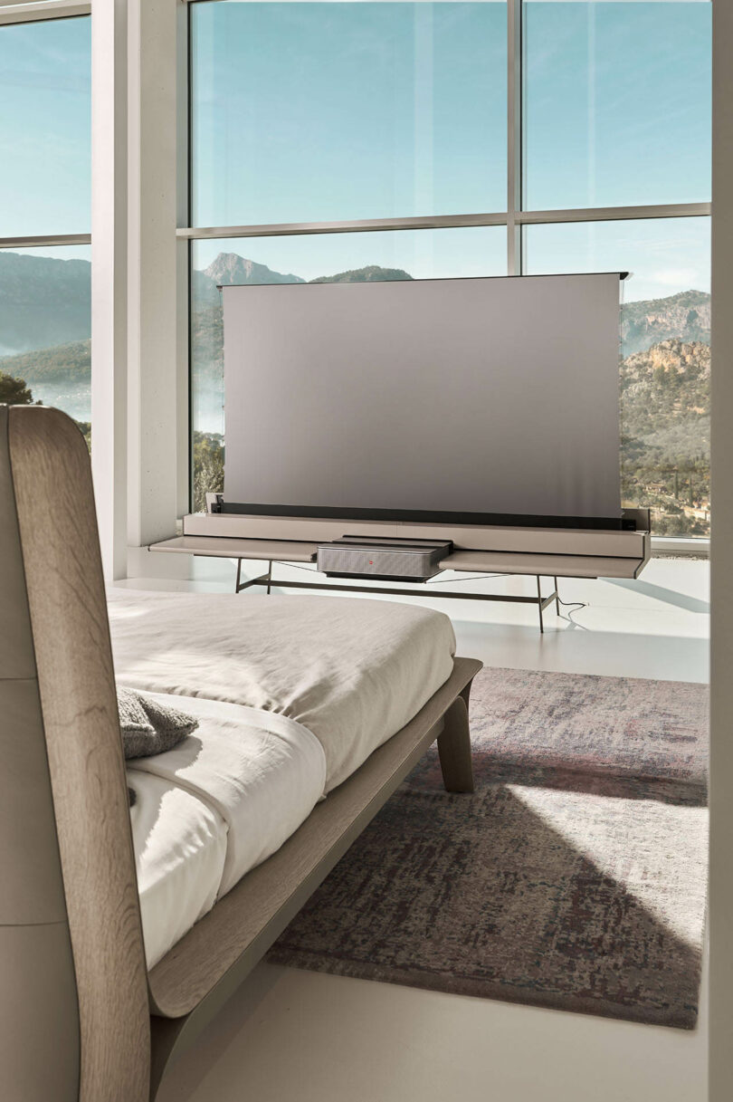 A modern bedroom featuring a low-profile media console with a screen partially raised at the foot of the bed.