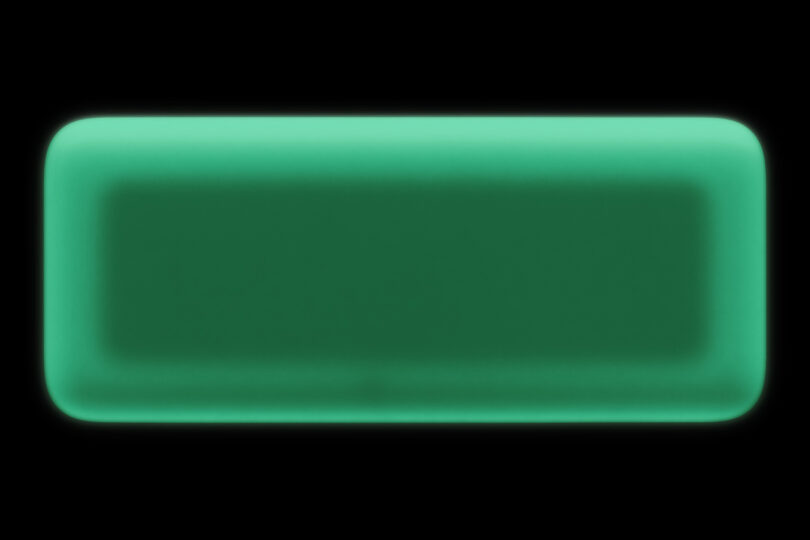 A rectangular device with rounded corners glowing in the dark against a black background.