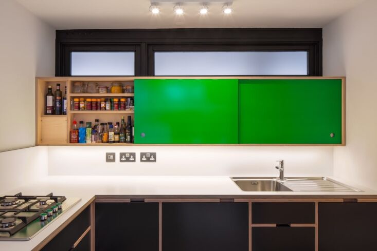 Shallow wooden shelving for spice jars and condiments against a bright green sliding door backdrop.