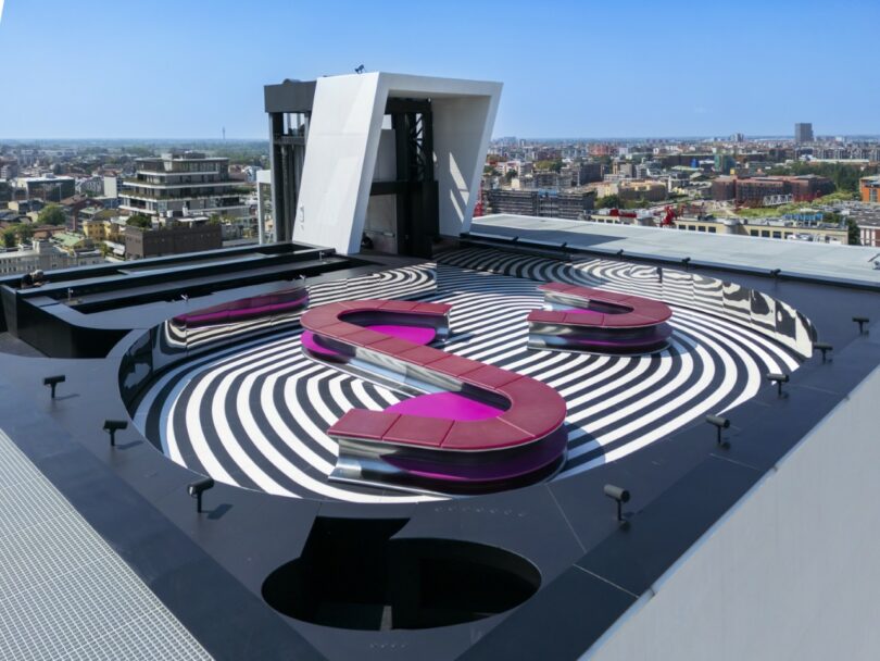 A pink S-shaped modular bench on a black and white spiraled floor pattern.