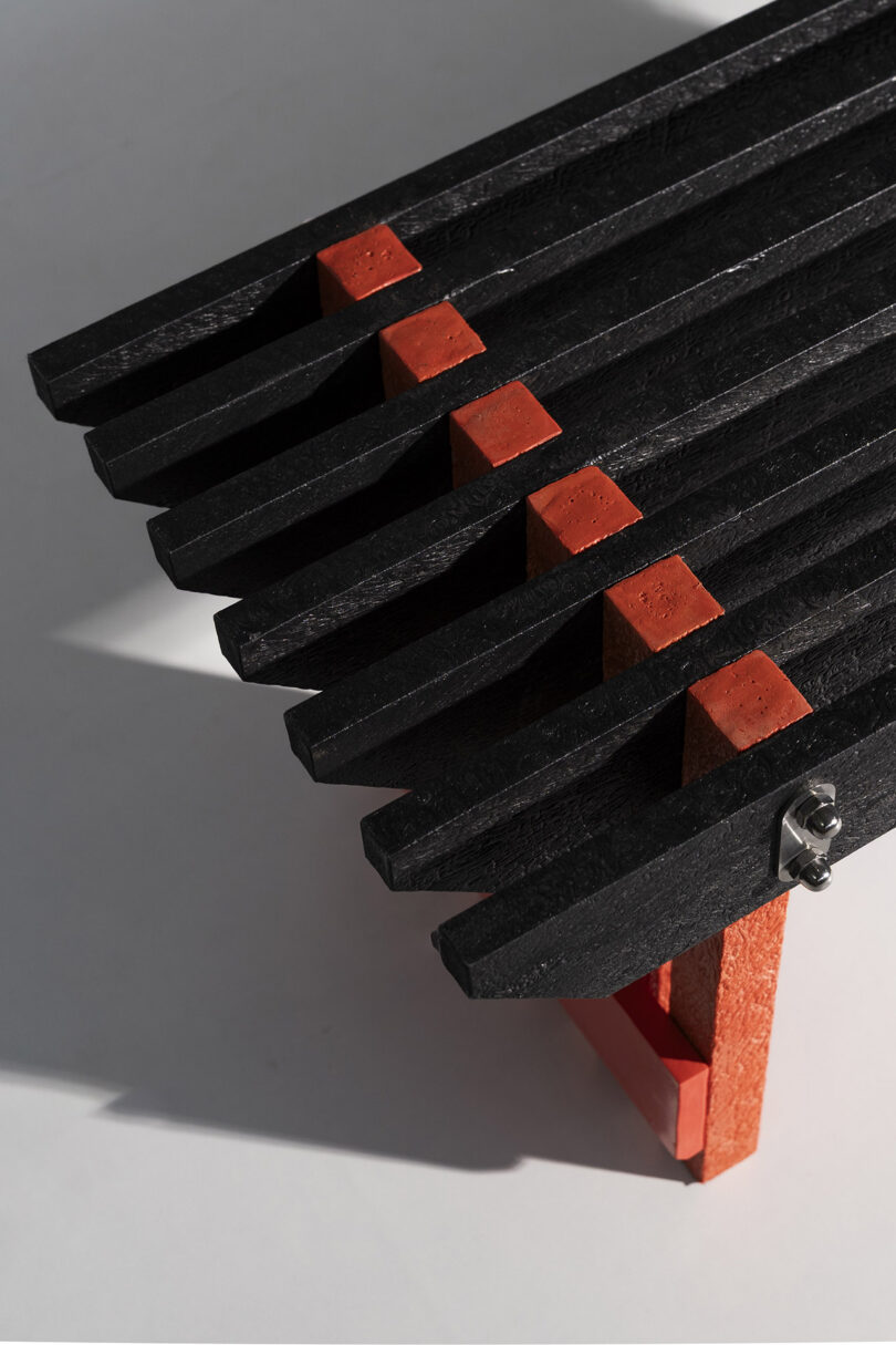 A close-up shot of the black recycled plastic slats and red supports of the Torii bench.