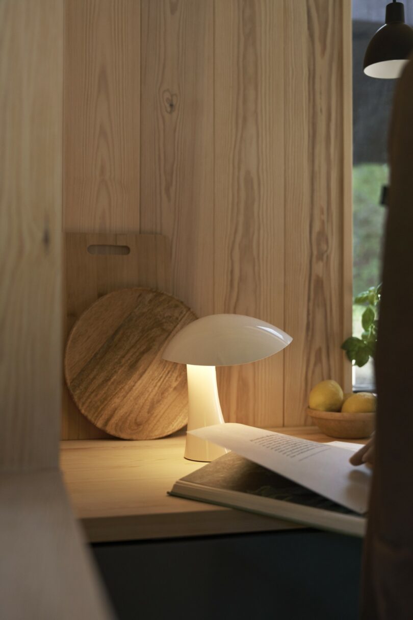 A white mushroom-shaped lamp on a wooden desk next to a book and lemons.