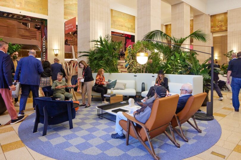 Indoor lounge area with comfortable armchairs, sofas, and indoor plants where people are relaxing and talking.