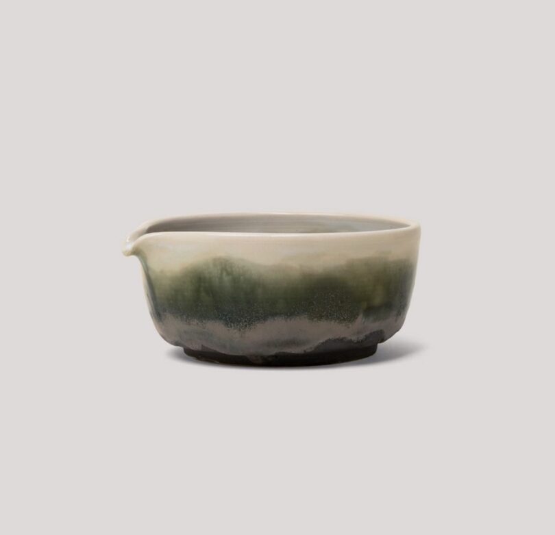 A handcrafted green and white gradient ceramic bowl with a small pouring spout.