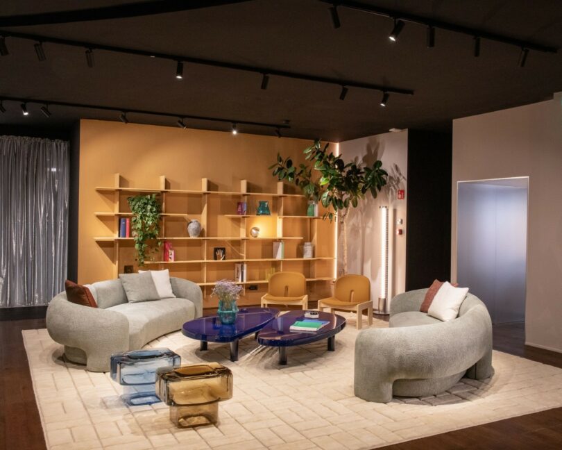 A living room interior featuring two amber side tables paired with a curved purple sofa against a mustard yellow wall.