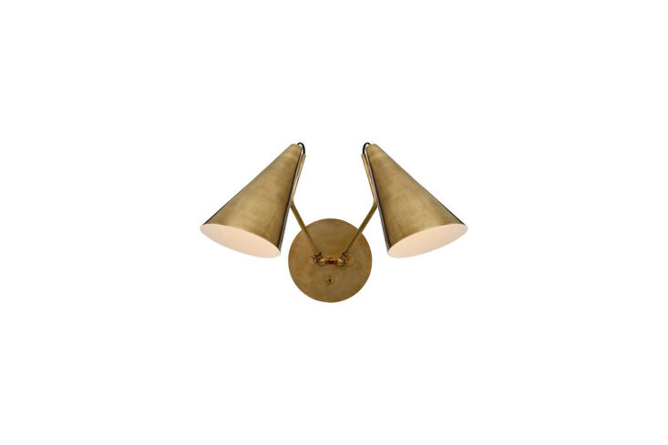 The Aerin Clemente Double Wall Sconce in antiqued brass mounted on a green wall.