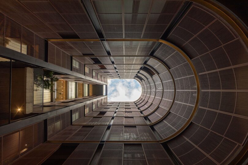 A dramatic upward view of a brutalist U-shaped atrium opening to a cloudy sky.