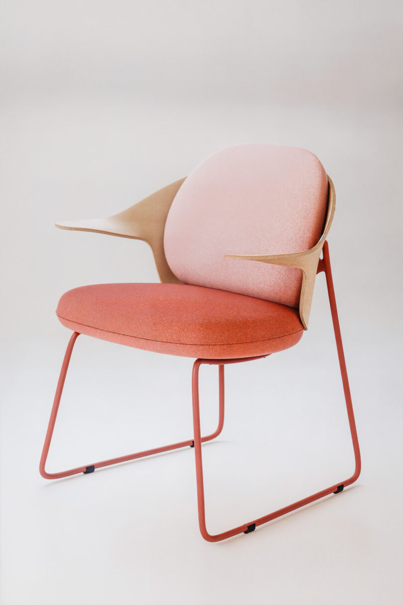 Modern Mysa chair with a pink cushioned seat, tan armrests, and a red metal frame.