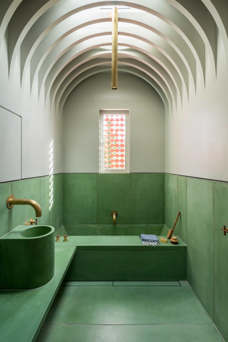 A pink-toned pigmented concrete hammam-style bathroom with a vaulted ceiling and brass shower fixtures.