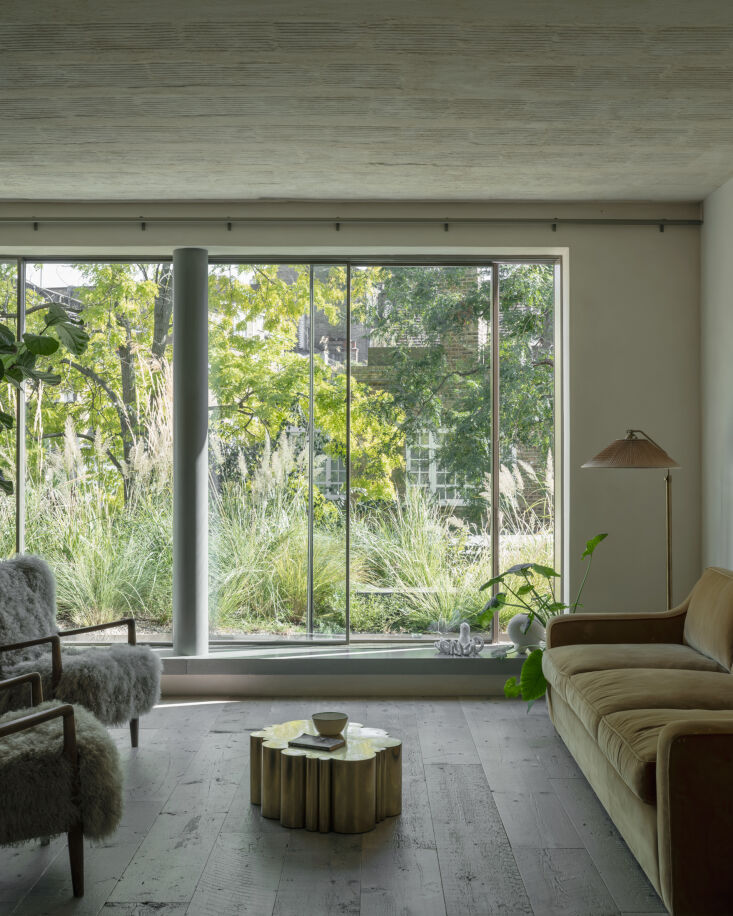 A modern living room with an exposed concrete ceiling, wooden floors, and soft blue upholstered seating.