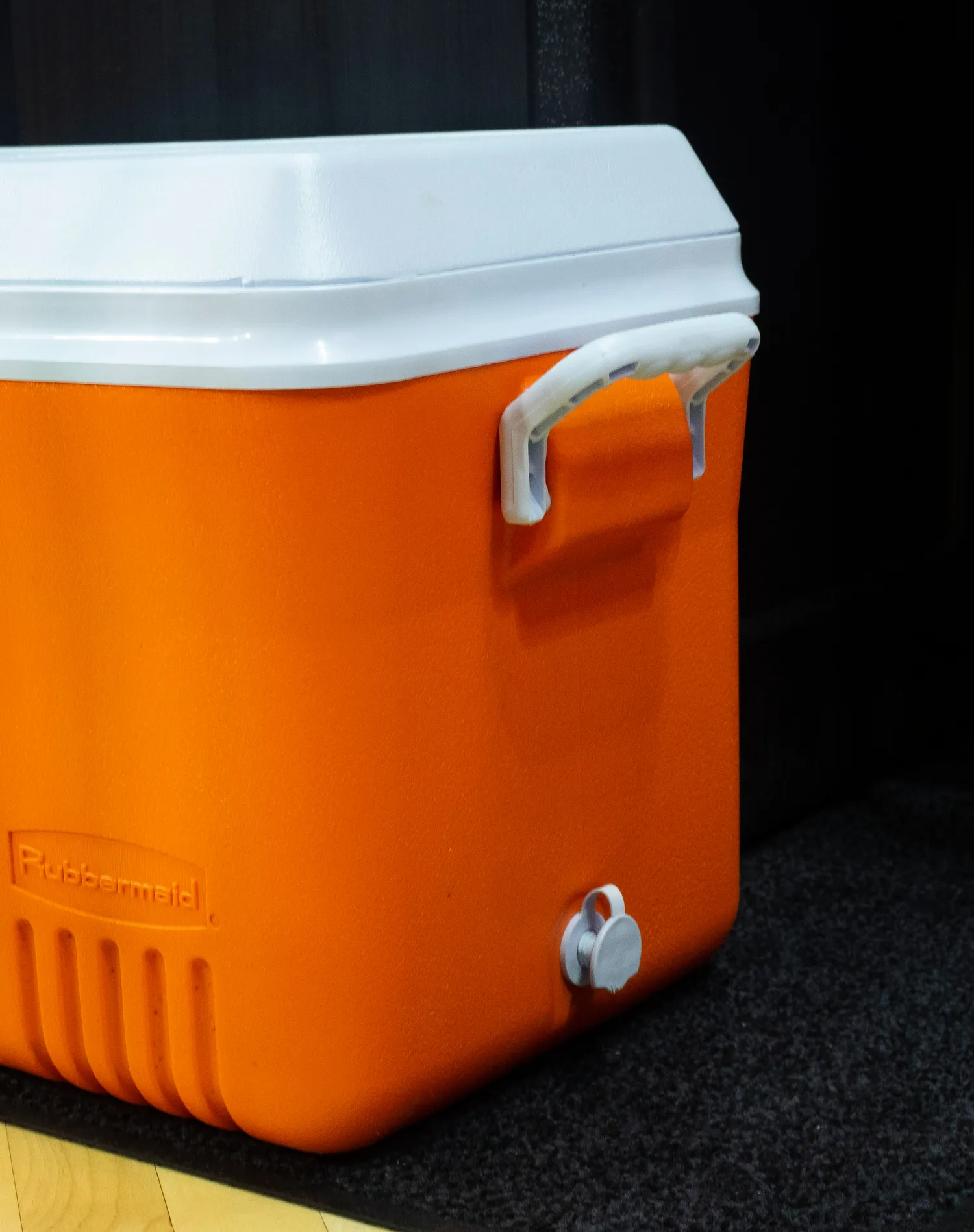 An orange plastic cooler with a white lid placed indoors on wooden flooring.