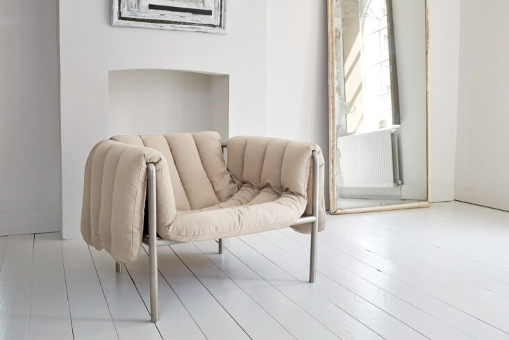 The Hem Puffy Lounge Chair with a thick, quilted beige seat draped over a simple stainless steel base.