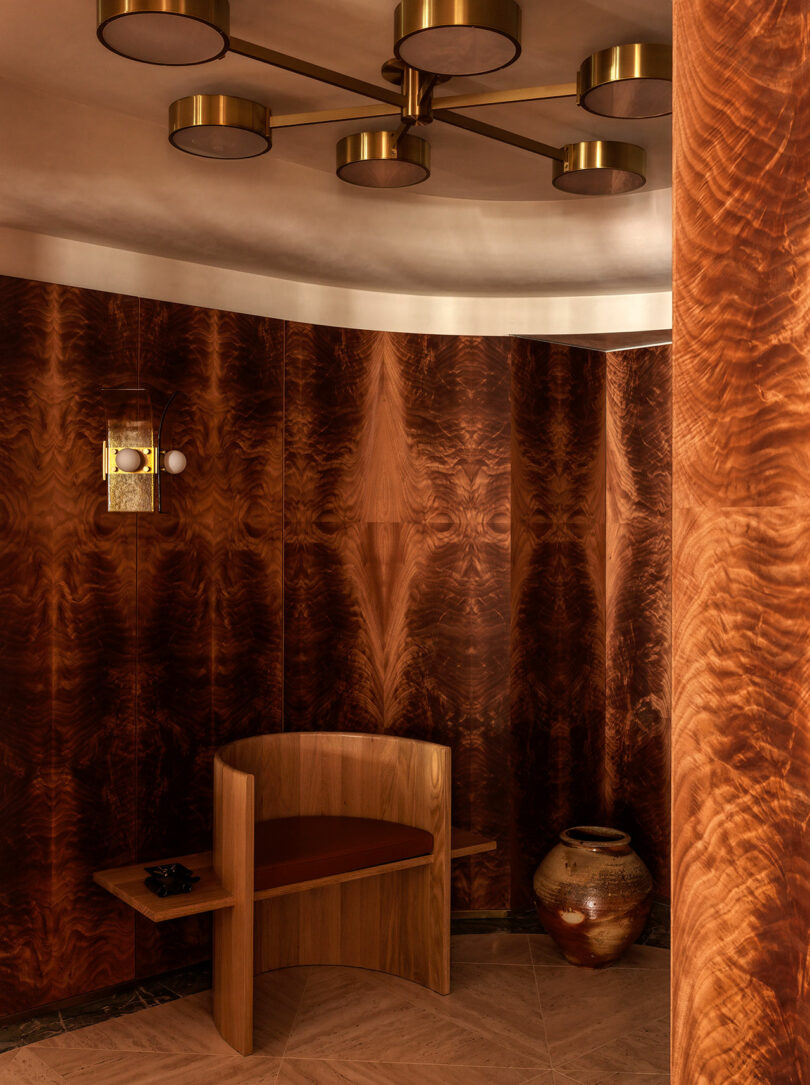A curved wood-paneled corner with a built-in bench and a minimalist brass light fixture.