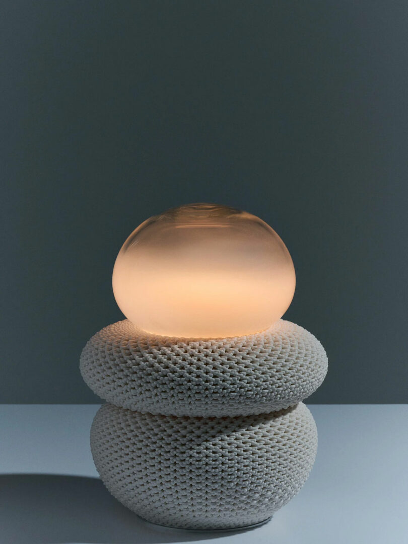 A modern designer lamp with a textured white 3D-printed ceramic base and a smooth glass orb top.