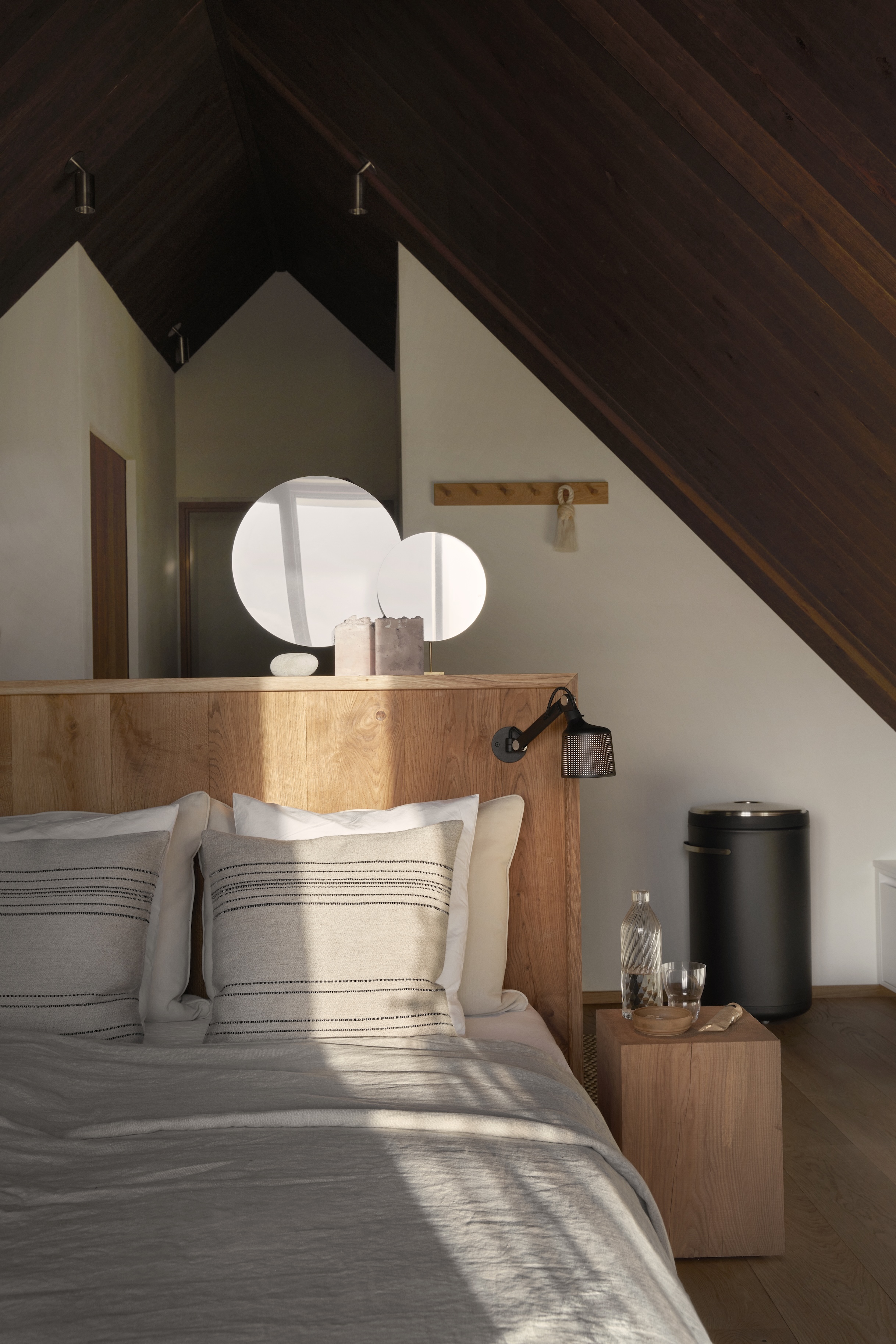 An attic bedroom with warm wood-paneled ceilings and a freestanding wooden headboard.