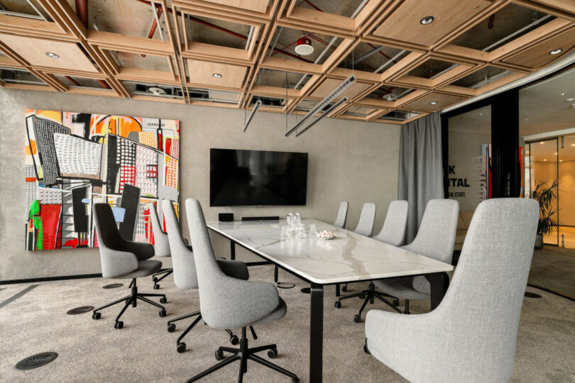 A sleek conference room featuring a long white table, gray chairs, and a slatted ceiling with LED lighting.