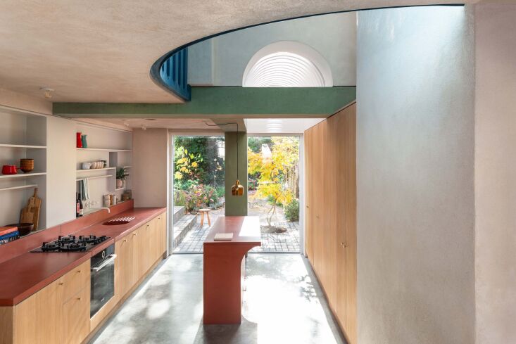 Interior of a double-height kitchen with vaulted louvered ceilings, a concrete island, and a mezzanine level.