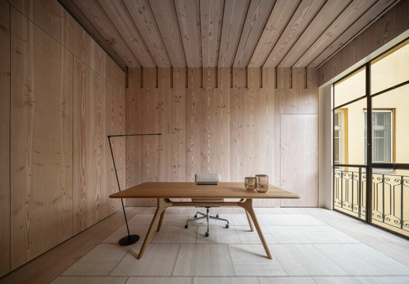 A modern home office setup with a wooden desk and chair integrated into a wood-paneled room.