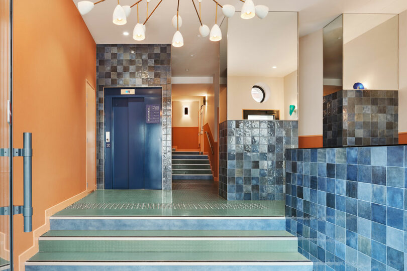 Modern building lobby with green tiled stairs, blue walls, and a contemporary elevator.