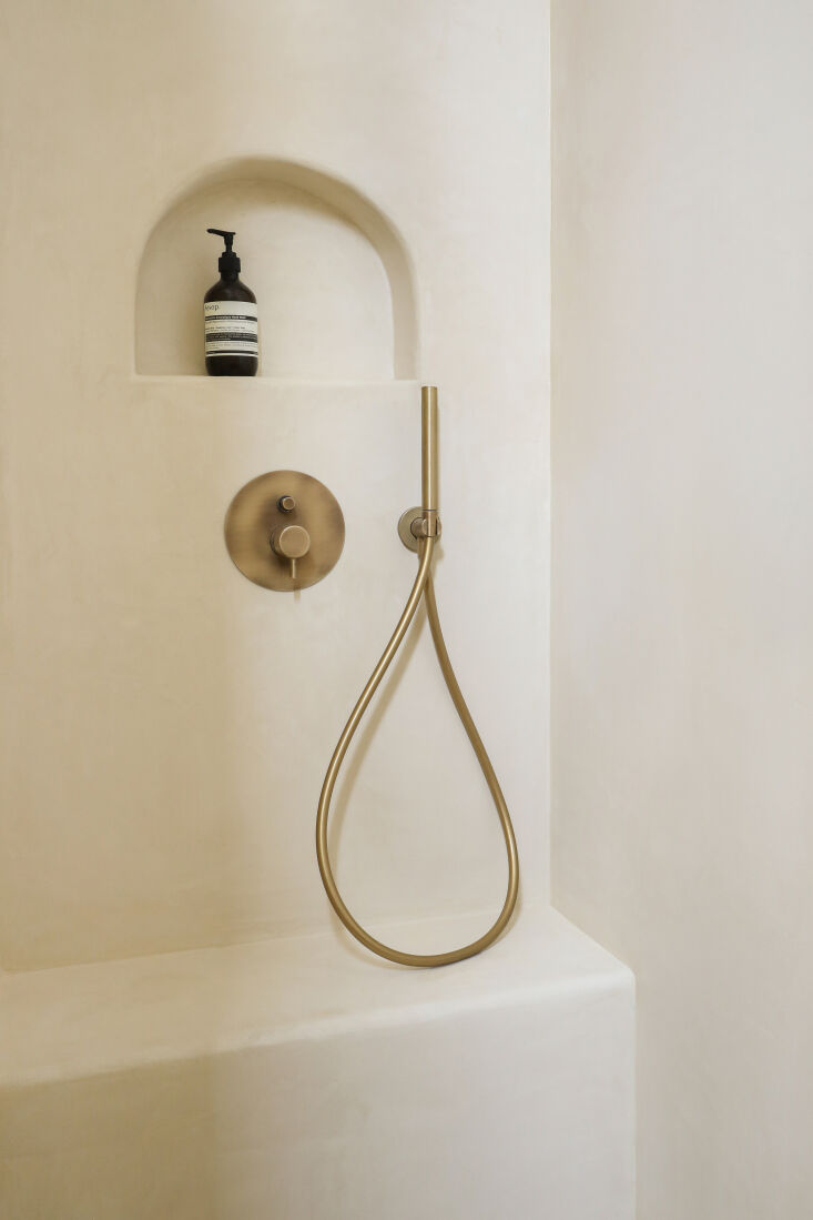 Minimalist bathroom with curved walls finished in smooth grey waxed concrete and a simple brass faucet.