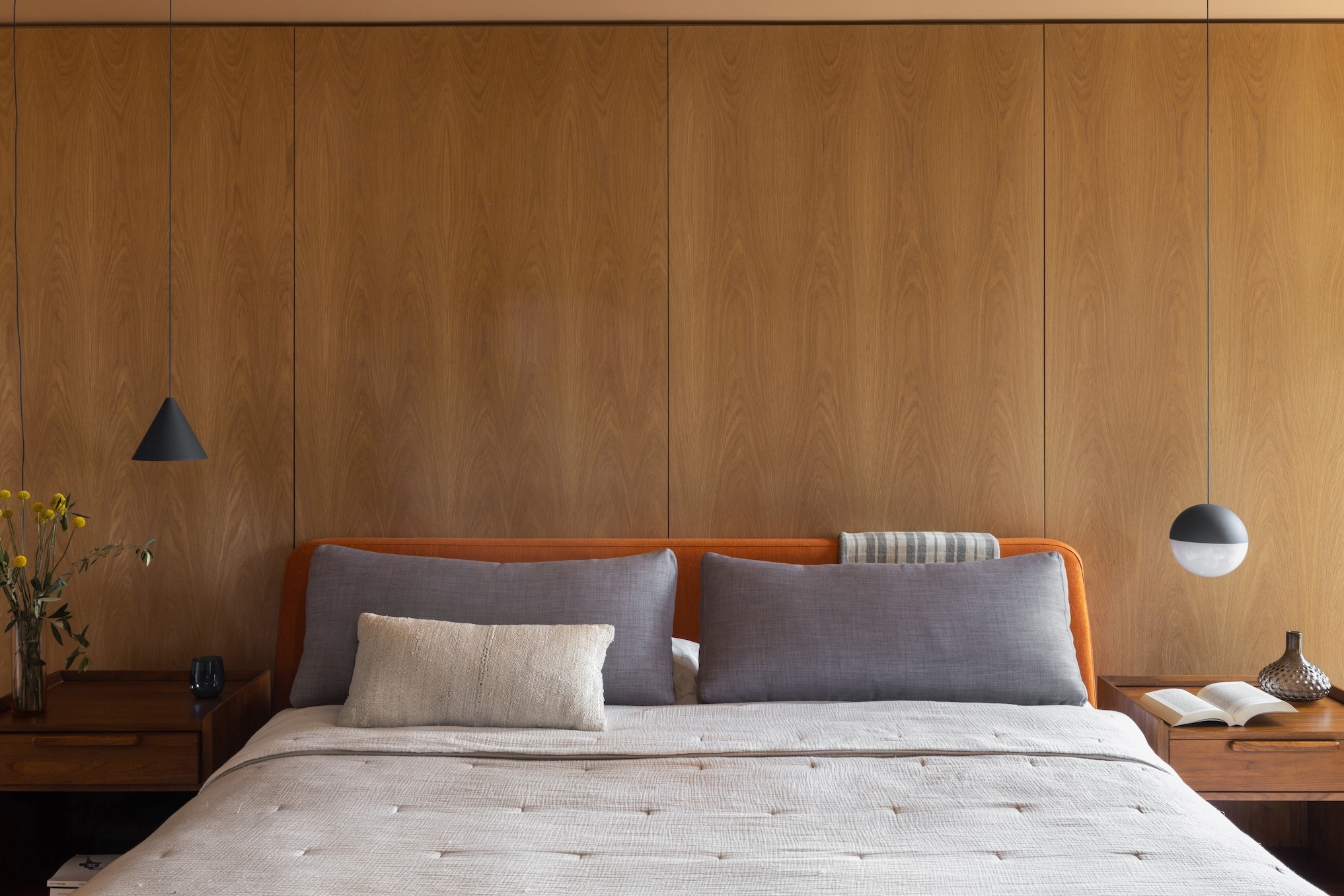 A primary bedroom featuring a central oak wall behind the bed with modern pendant lighting.