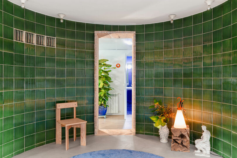Interior view of an apartment with green ceramic tiles and a stone doorway leading to lush indoor plants.
