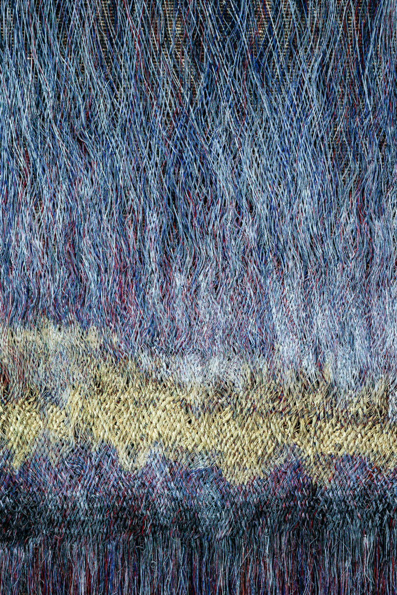 Close-up of a woven textile featuring wave-like patterns of blue, red, and tan threads.