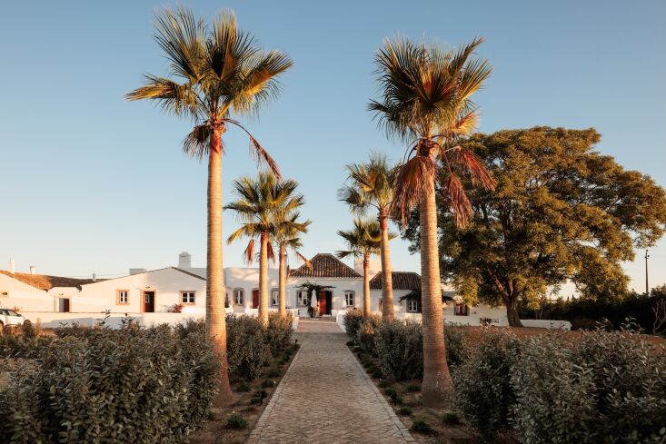 White stucco farm buildings with original terracotta-tiled roofs under a clear blue sky.