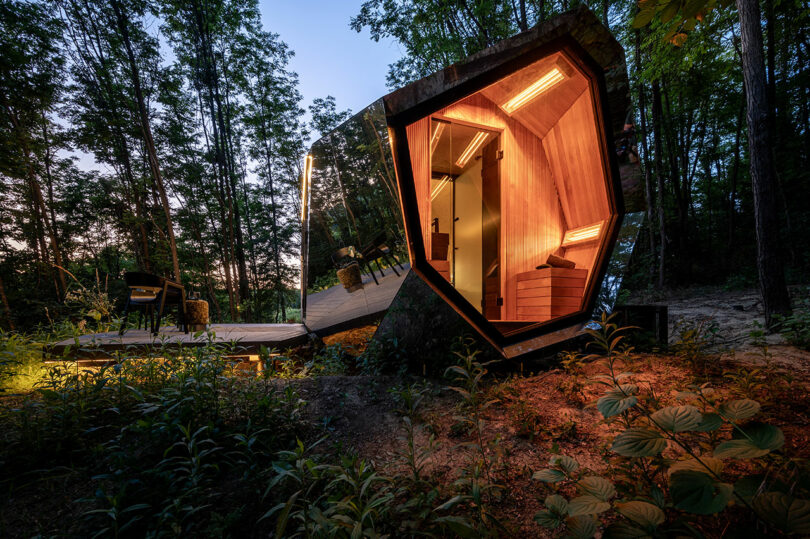 An illuminated PEBL Grand cabin with a warm wooden interior sitting in a dark forest at dusk.
