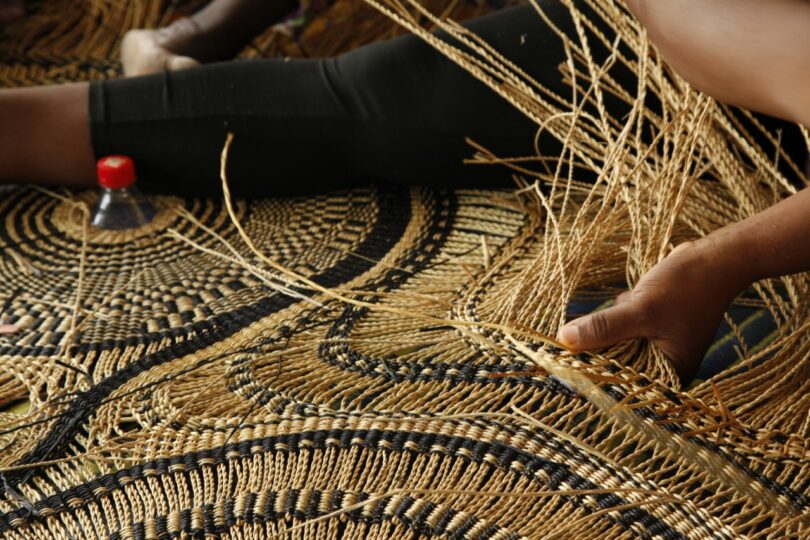 Detailed view of an artisan's hands weaving natural fibers into a complex pattern.