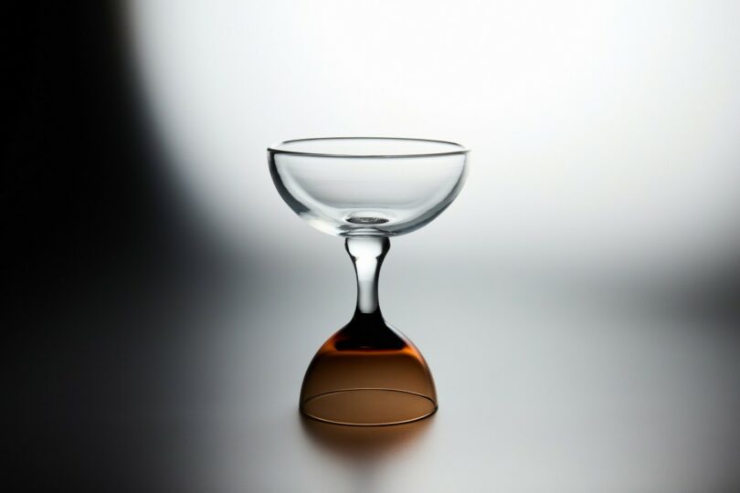 A clear glass coupe with a distinct brown or copper-colored base.
