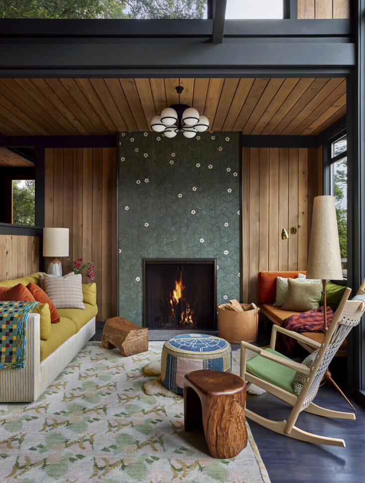 Vertical cedar wood paneling surrounding a dark-trimmed fireplace with ornamental glass tiles.