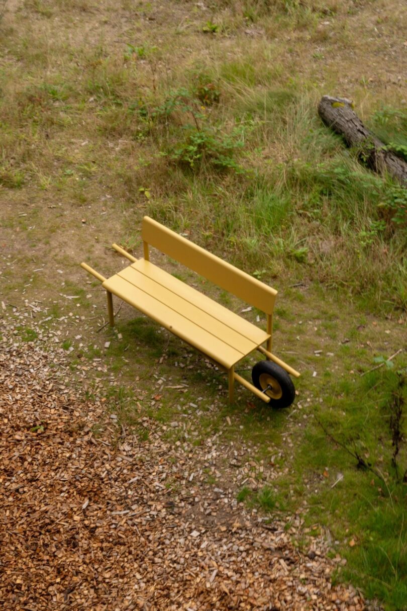 Full view of a yellow metal Wheelbench on grass showing its wheelbarrow-style handles and single front wheel.
