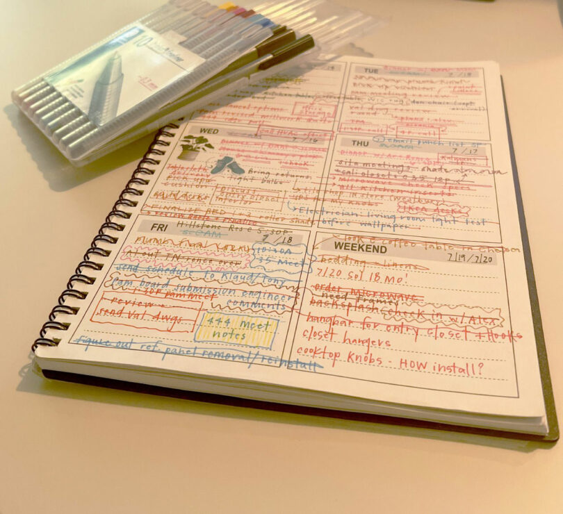 An open paper planner with detailed handwritten notes and colored pens on a desk.
