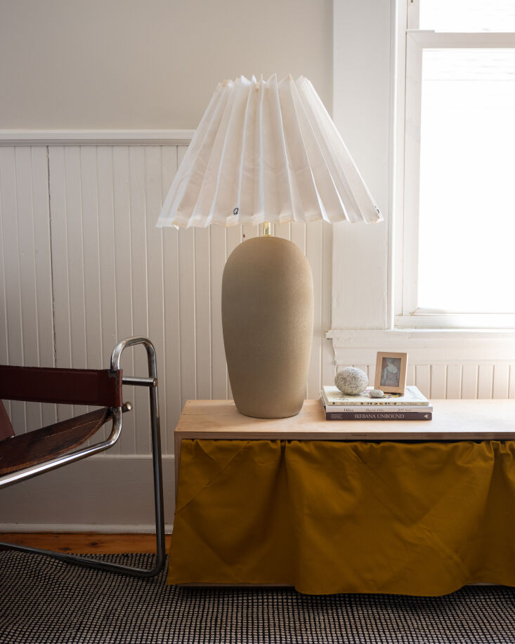 A finished white pleated lampshade on a vintage ceramic base in a cozy living room.